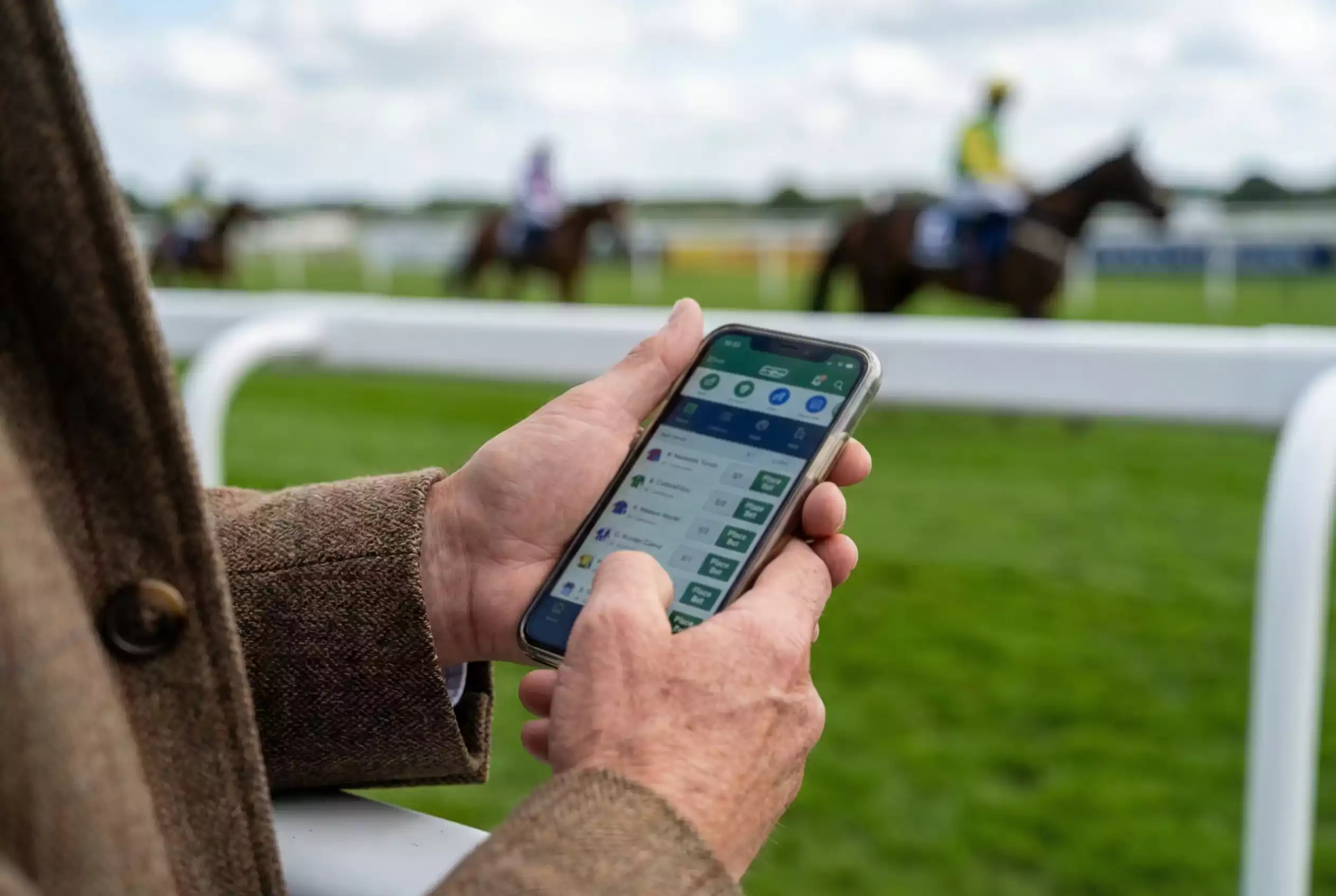 Person placing each-way bet on smartphone with racecourse in background